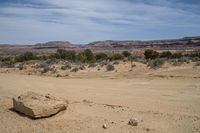 a large rock on the ground in front of a desert mountain and some trees with rocks