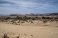 a large rock on the ground in front of a desert mountain and some trees with rocks