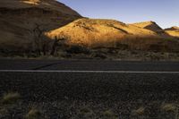 a lone road in the desert under mountains, surrounded by barren terrain with no trees