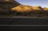 a lone road in the desert under mountains, surrounded by barren terrain with no trees