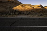 a lone road in the desert under mountains, surrounded by barren terrain with no trees