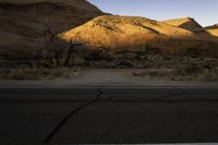 a lone road in the desert under mountains, surrounded by barren terrain with no trees