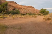 a person on a motorcycle rides down the dirt road near tall red rocks and trees