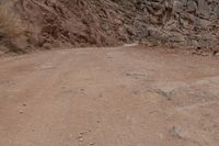 a dirt road and a large cliff face down the side of it that has a small red bus parked on the side of it