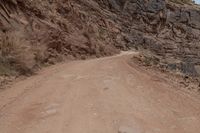 a dirt road and a large cliff face down the side of it that has a small red bus parked on the side of it