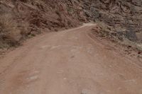 a dirt road and a large cliff face down the side of it that has a small red bus parked on the side of it