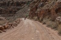 a dirt road and a large cliff face down the side of it that has a small red bus parked on the side of it