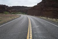 a person riding a motorcycle along a narrow road through rocks and sand cliffs a grassy area on both sides