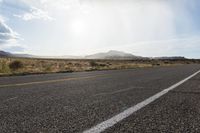 an empty street with mountains and dirt in the background with sunbeaming over the horizon