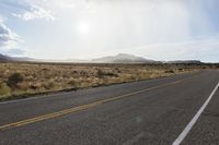 an empty street with mountains and dirt in the background with sunbeaming over the horizon