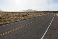 an empty street with mountains and dirt in the background with sunbeaming over the horizon