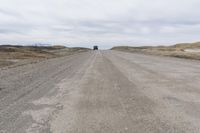 a vehicle driving down a gravel road with a cloudy sky above it in an open area