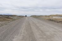 a vehicle driving down a gravel road with a cloudy sky above it in an open area