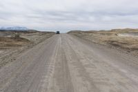 a vehicle driving down a gravel road with a cloudy sky above it in an open area