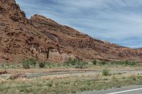 view of rocky cliff along the desert road from side of truck window, on partly sunny day