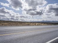 a lone motorcycle parked on the side of a road under a cloudy sky in the desert