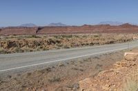 a long curved road with some rocks on both sides of it in the desert, along with hills and scrub