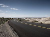 a paved road in the middle of a mountain valley is seen as a view across an arid plain, with no cars on it