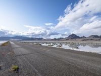 an empty street and a lake in the middle of the desert, with a cloudy sky