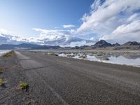 an empty street and a lake in the middle of the desert, with a cloudy sky