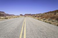 the road in desert is wide and empty with sparse brush, mountains and sand on either side