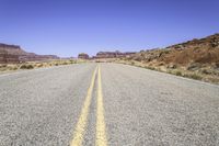 the road in desert is wide and empty with sparse brush, mountains and sand on either side