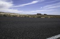 the asphalt of a street in a large desert area with mountains in the distance and a lone red sign in front