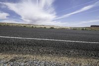 the asphalt of a street in a large desert area with mountains in the distance and a lone red sign in front