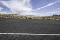 the asphalt of a street in a large desert area with mountains in the distance and a lone red sign in front