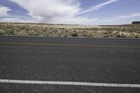 the asphalt of a street in a large desert area with mountains in the distance and a lone red sign in front