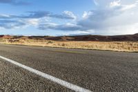 a bike rider rides down a paved desert road in the desert near mountains and clouds