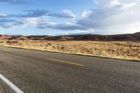 a bike rider rides down a paved desert road in the desert near mountains and clouds