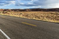 a bike rider rides down a paved desert road in the desert near mountains and clouds