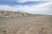 an empty road is shown on the edge of a desert plain with low shrubs and blue skies above it