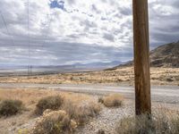 an old utility pole in a desert landscape next to a dirt road with mountains in the background