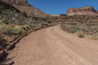 a dirt road winding up a desert like area with rocky cliffs in the distance behind it