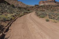 a dirt road winding up a desert like area with rocky cliffs in the distance behind it