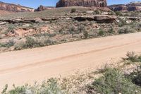 a motor vehicle driving in front of rocks and shrubs in the desert area of a mountain range