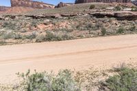 a motor vehicle driving in front of rocks and shrubs in the desert area of a mountain range