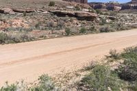 a motor vehicle driving in front of rocks and shrubs in the desert area of a mountain range