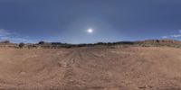 a wide angle view of a dirt road in desert conditions and the sun setting through