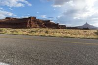 the road winds away from a mountain in a valley surrounded by rocks and tall grass