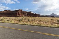 the road winds away from a mountain in a valley surrounded by rocks and tall grass