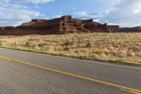 the road winds away from a mountain in a valley surrounded by rocks and tall grass