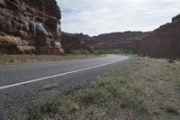 a person riding a motorcycle along a narrow road through rocks and sand cliffs a grassy area on both sides