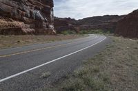 a person riding a motorcycle along a narrow road through rocks and sand cliffs a grassy area on both sides