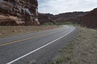 a person riding a motorcycle along a narrow road through rocks and sand cliffs a grassy area on both sides