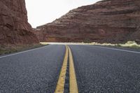 a person riding a motorcycle along a narrow road through rocks and sand cliffs a grassy area on both sides