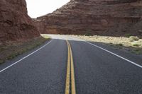 a person riding a motorcycle along a narrow road through rocks and sand cliffs a grassy area on both sides