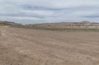 an empty field next to a big mountain with rocks in the background of the picture